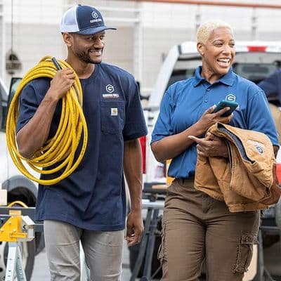 Construction crew in navy branded work shirts and vests carrying tools and lumber past their work van