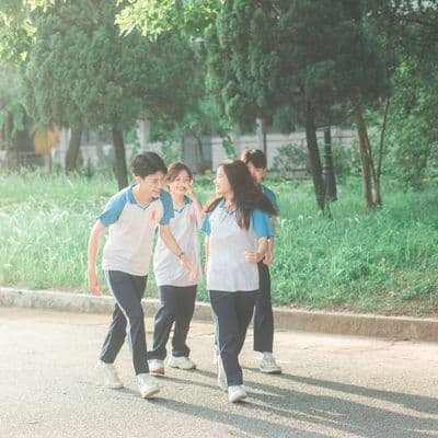 Four students in matching blue and white school shirts walking together along a tree-lined path
